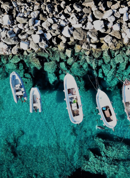 Barche ancorate in acque cristalline vicino a una costa rocciosa.