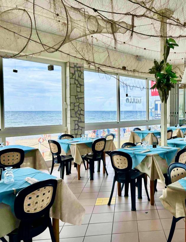 Seaside restaurant with set tables and Italian flags.