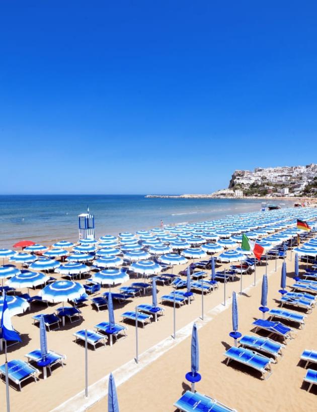 Spiaggia attrezzata con ombrelloni blu e vista su un borgo costiero.